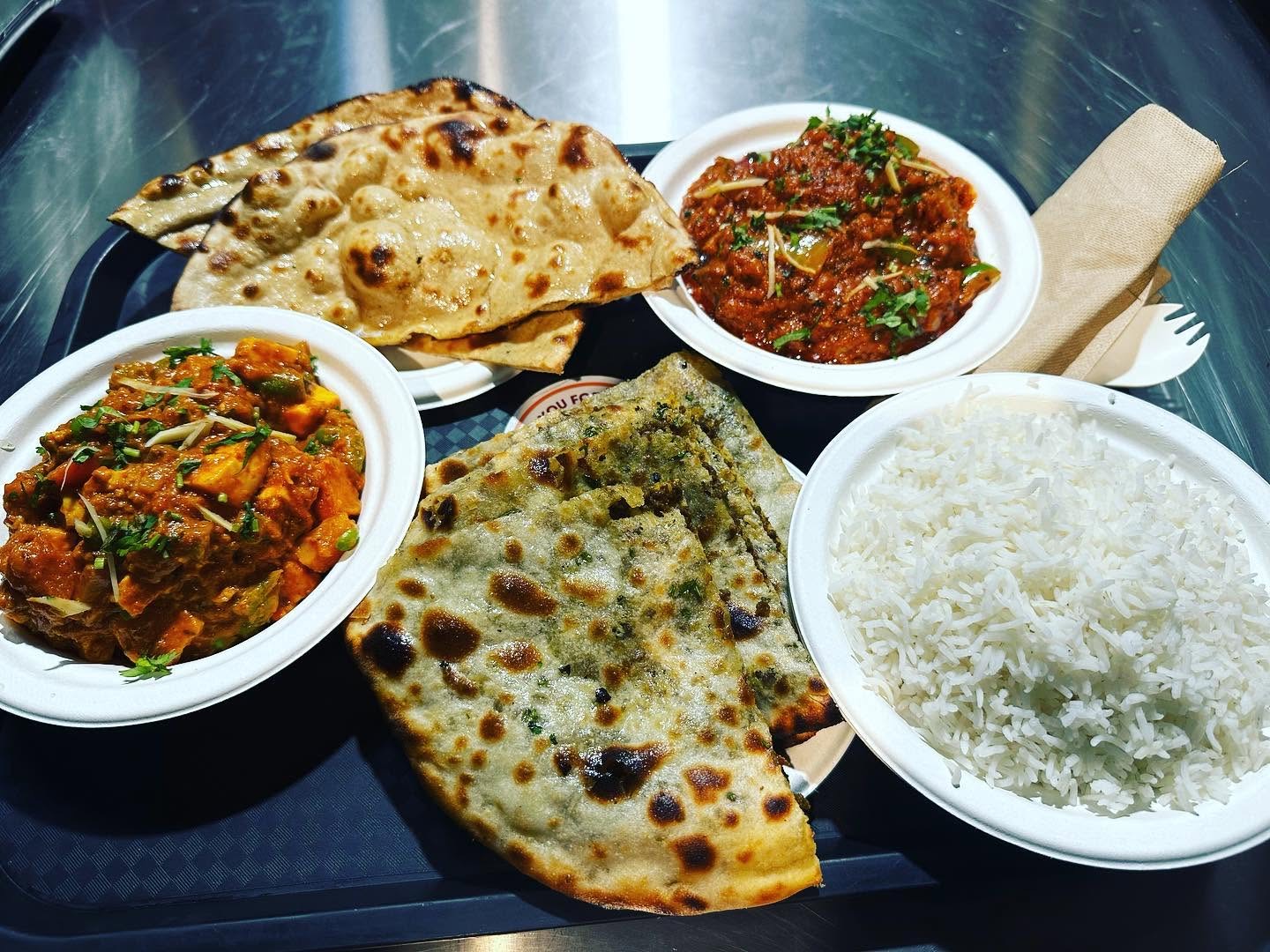 Naan, paneer curry, chicken curry and rice on a tray